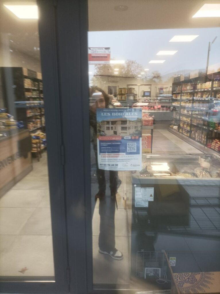 hôtesse qui colle une affiche dans une affiche sur la vitrine d'un commerce de Saint-Maximin-la-sainte-Baume